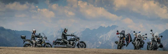 Motorradfahrer mit ihren Motorrädern vor Bergkulisse unter bewölktem Himmel
