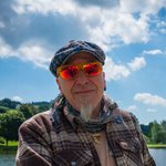 Mann mit roter Sonnenbrille vor Fluss und blauem Himmel