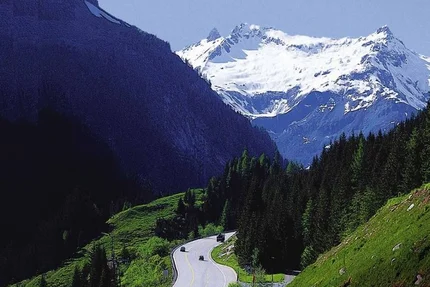 Mountain road with cars, green forests, and snow-covered peaks