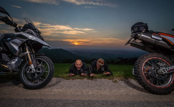 Motorvakantie in het Mühlviertel © Moppetfoto.de Twee mannen liggen op gras tussen motoren bij zonsondergang