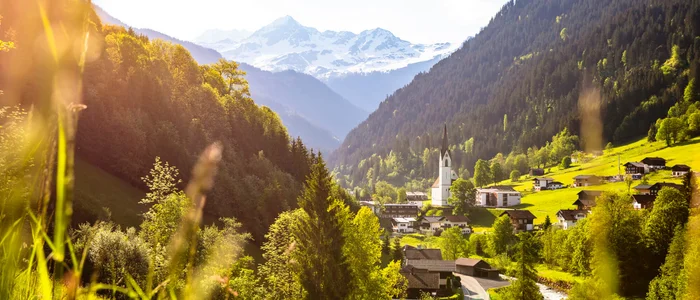 Idyllisches Tal mit Dorf, Kirche und schneebedeckten Bergen im Sonnenschein