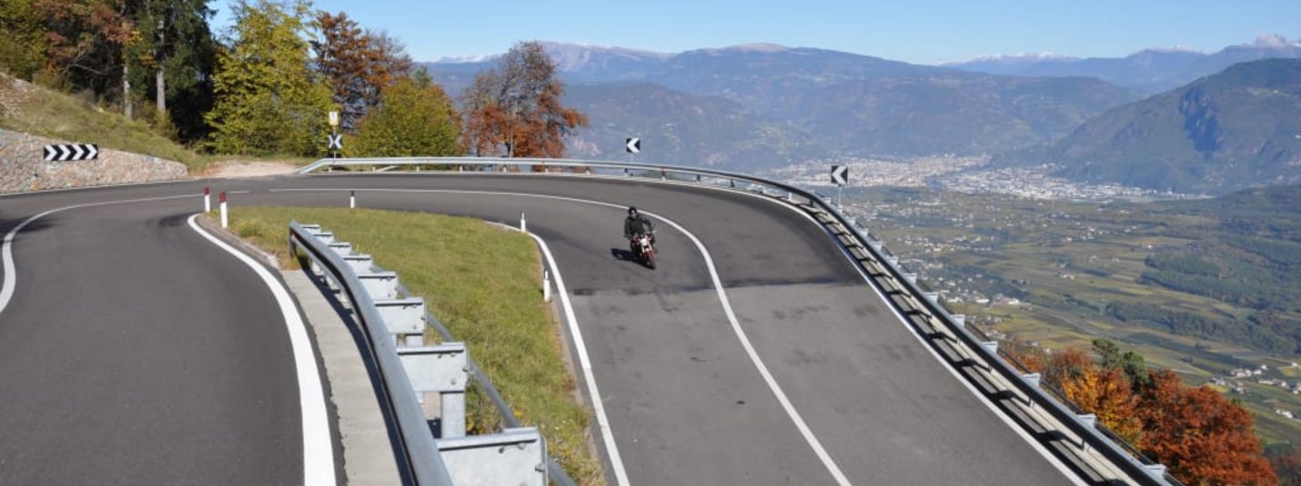Kurvige Bergstraße mit Motorradfahrer und Blick auf Tal und Berge