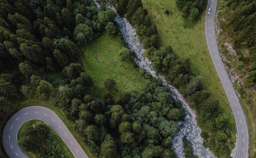 Luftaufnahme einer kurvigen Straße neben einem Bach und Wald