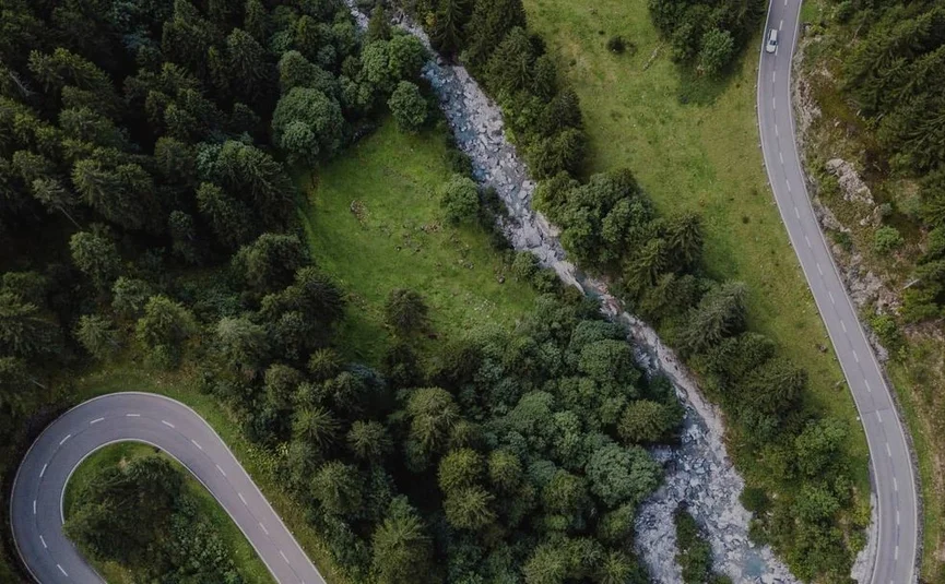 Luftaufnahme einer kurvigen Straße neben einem Bach und Wald