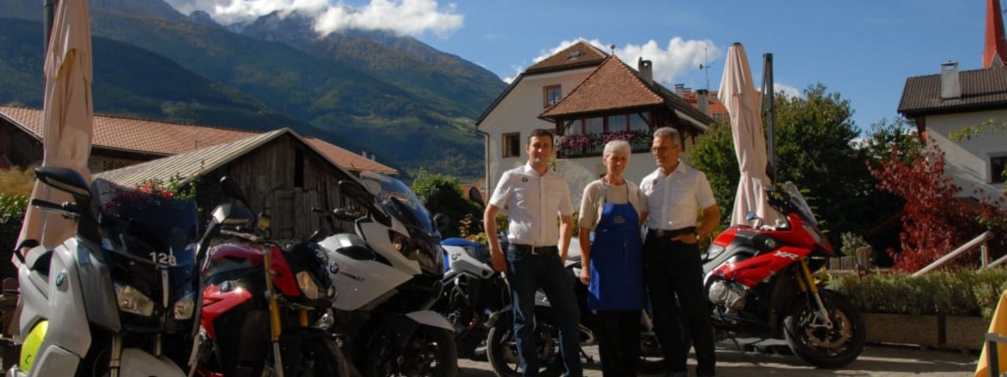 Drei Personen stehen vor mehreren BMW Motorrädern in einer Berglandschaft
