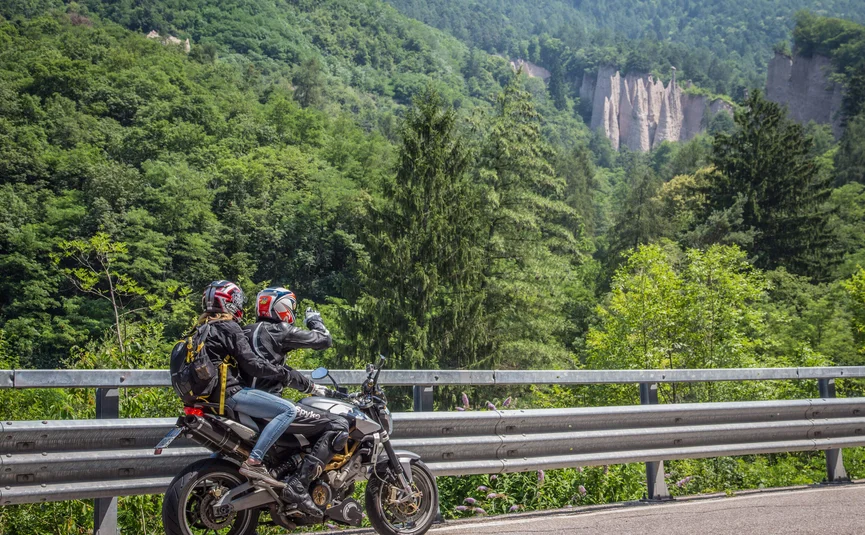 Motorradurlaub im Val di Fiemme © A. Monticelli Zwei Motorradfahrer halten an einer Straße, im Hintergrund Wald und Felsformationen