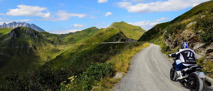 Motorradfahrer auf Bergstraße mit grünen Hügeln und blauem Himmel