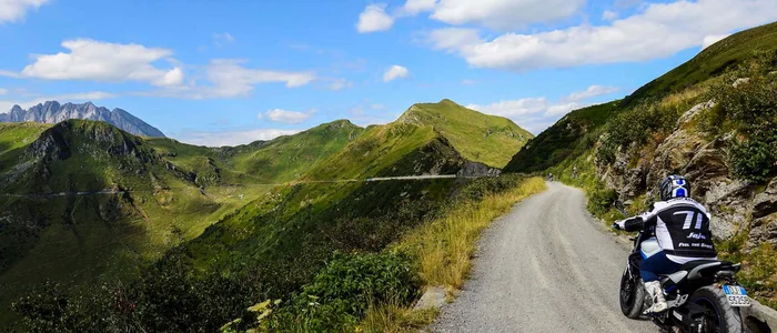 Motorradfahrer auf Bergstraße mit grünen Hügeln und blauem Himmel