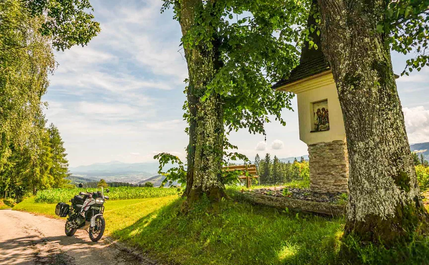 Motorcycle beside chapel and trees on a sunny rural path
