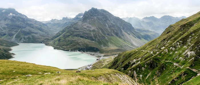 Bergsee und grüne Alpenhänge bei bewölktem Himmel