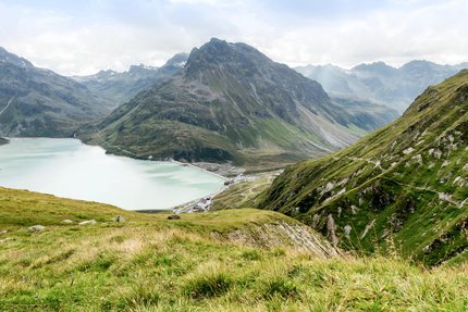 Bergsee und grüne Alpenhänge bei bewölktem Himmel