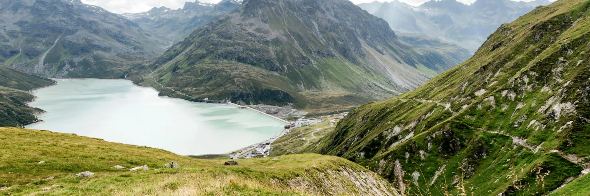 Mountain lake and green alpine slopes under cloudy sky