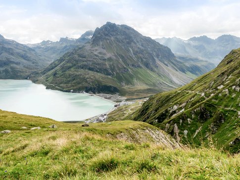 Mountain lake and green alpine slopes under cloudy sky