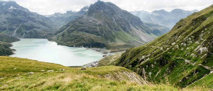 Bergsee und grüne Alpenhänge bei bewölktem Himmel
