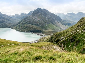 Bergsee und grüne Alpenhänge bei bewölktem Himmel