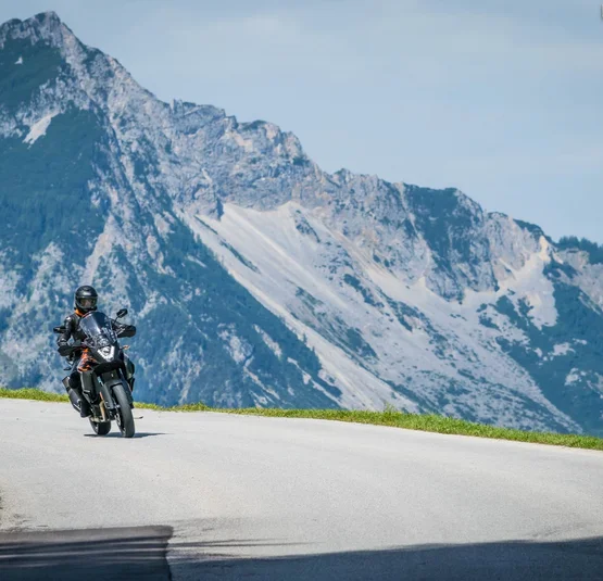 Motorcyclist riding on mountain road with steep rocky mountains in background