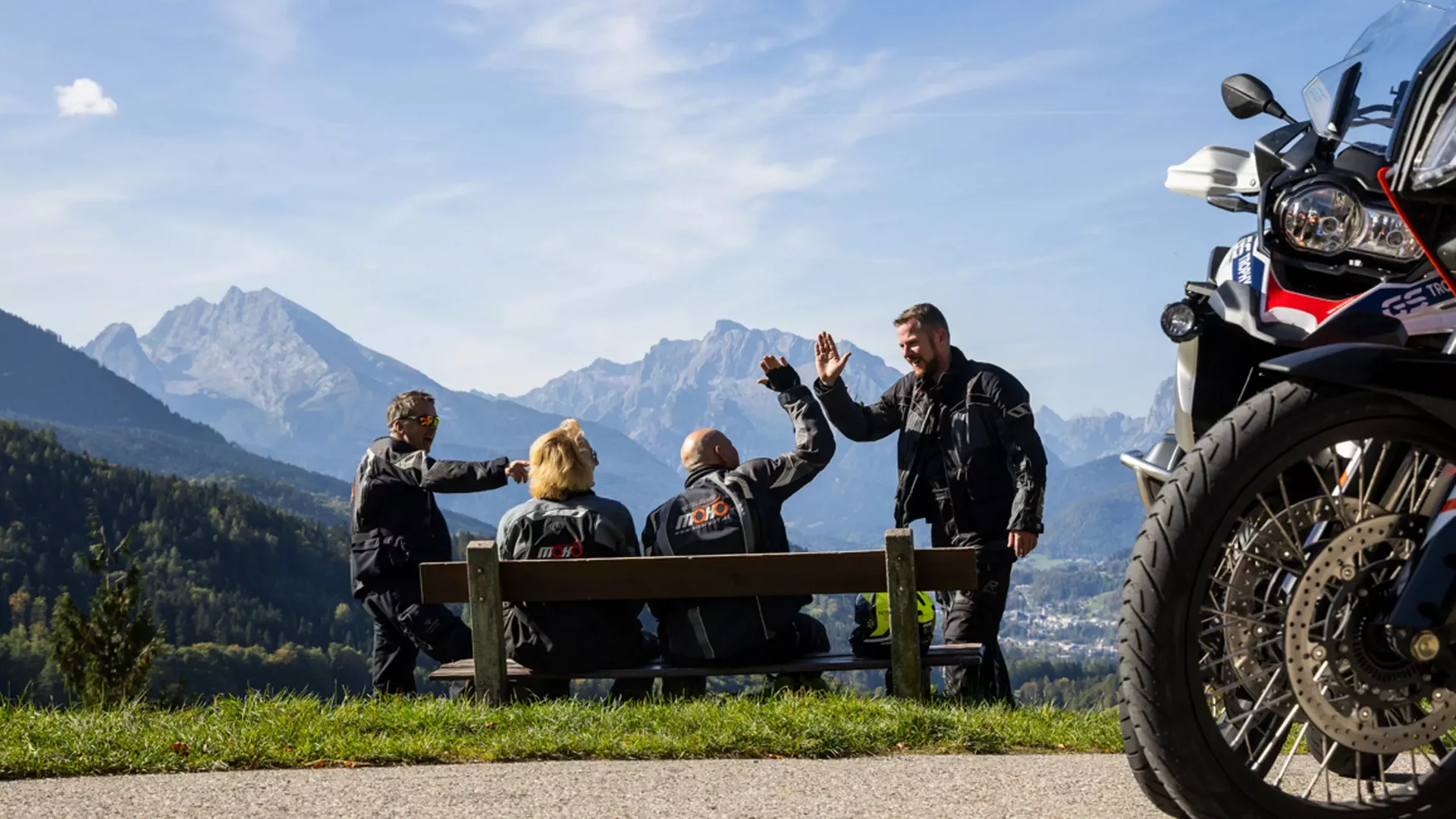 Urlaubsberater © Heiko Mandl Motorradfahrer begrüßen sich auf Bank mit Bergblick