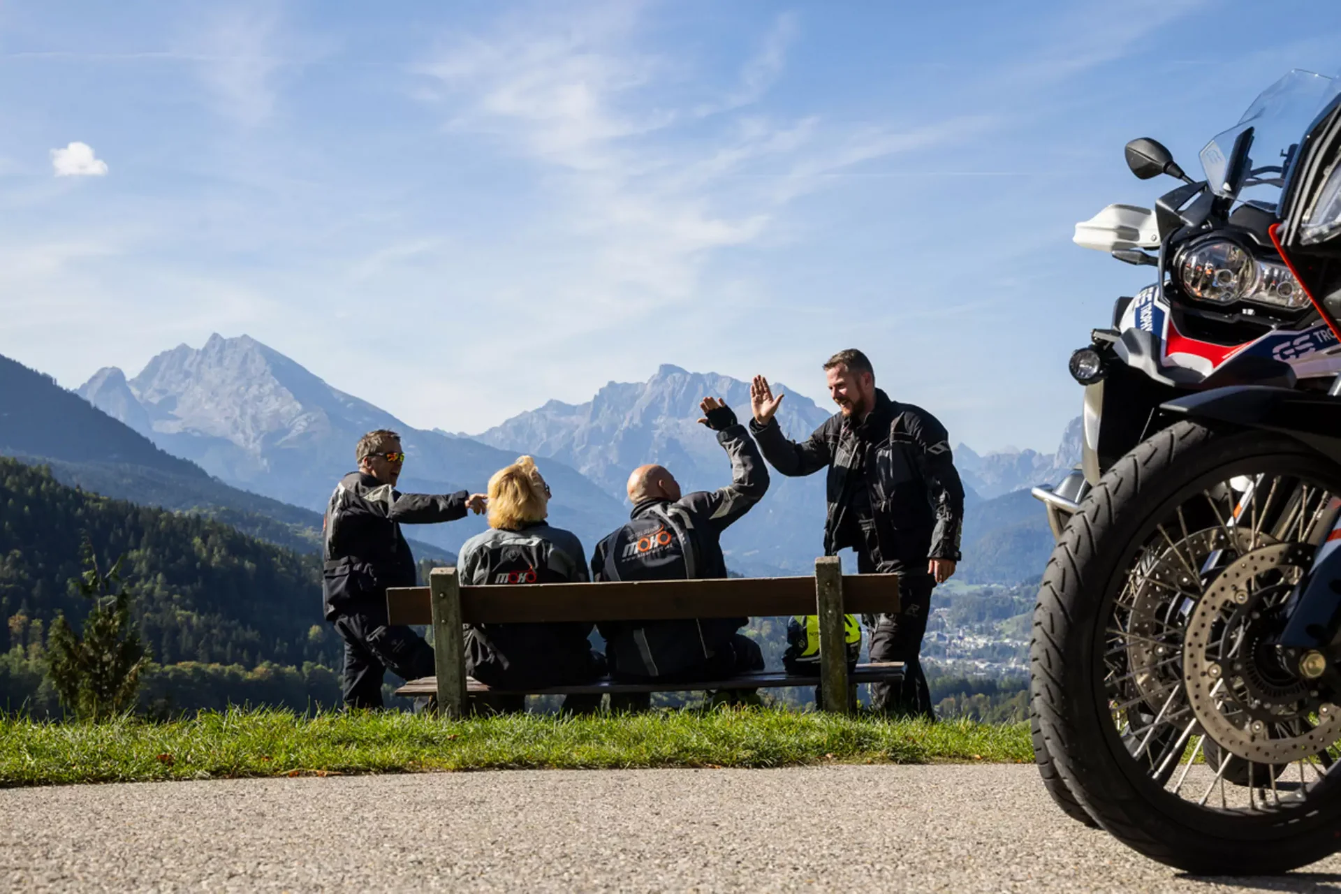 Motorradurlaub © Heiko Mandl Motorradfahrer begrüßen sich auf Bank mit Bergblick