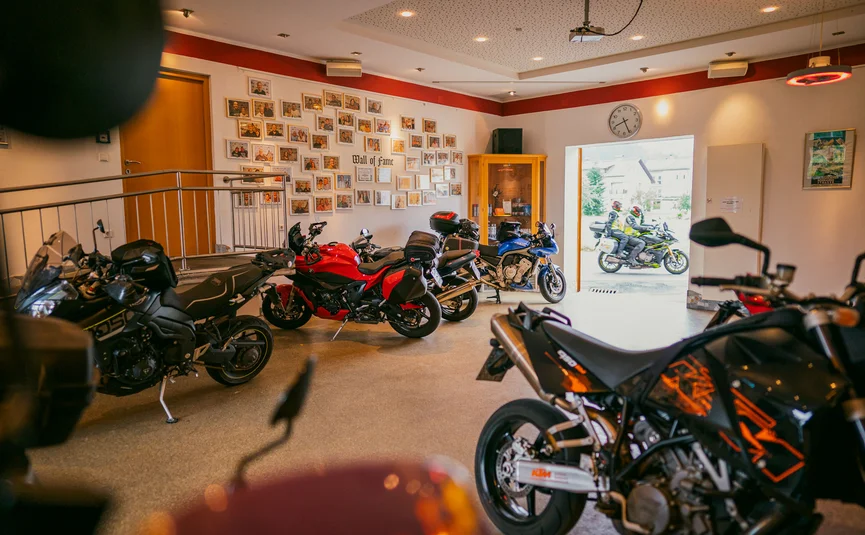 Several motorcycles inside a room with open door showing two riders outside