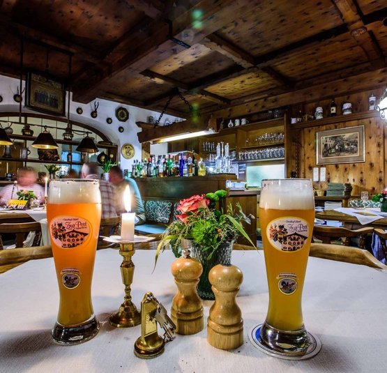 Zwei Biergläser und Kerze in rustikalem Gastraum mit Holzdach