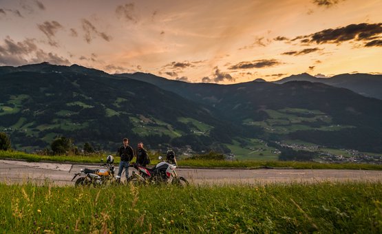 Motorradurlaub in Tirol © Moppetfoto.de Zwei Männer mit Motorrädern auf Straße bei Sonnenuntergang in bergiger Landschaft
