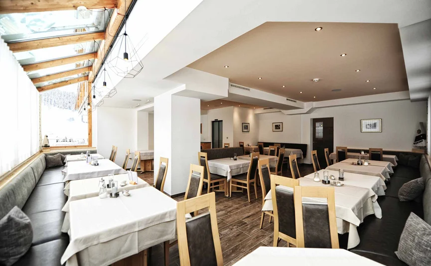 Leerer moderner Speisesaal mit Holzmöbeln und weißen Tischdecken.