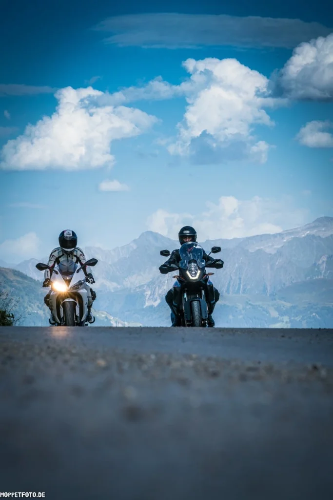 Zwei Motorradfahrer auf Bergstraße vor bewölktem Himmel