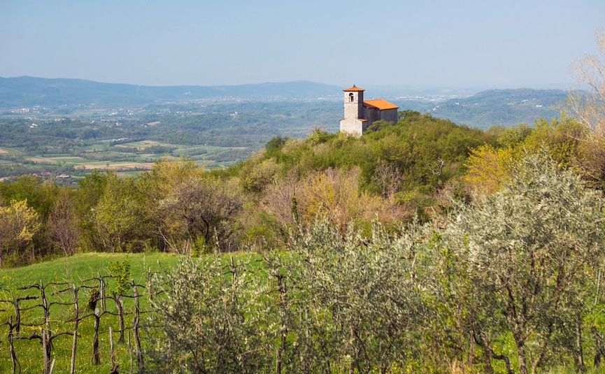 Kerk op een beboste heuvel met vallei en bergen op de achtergrond
