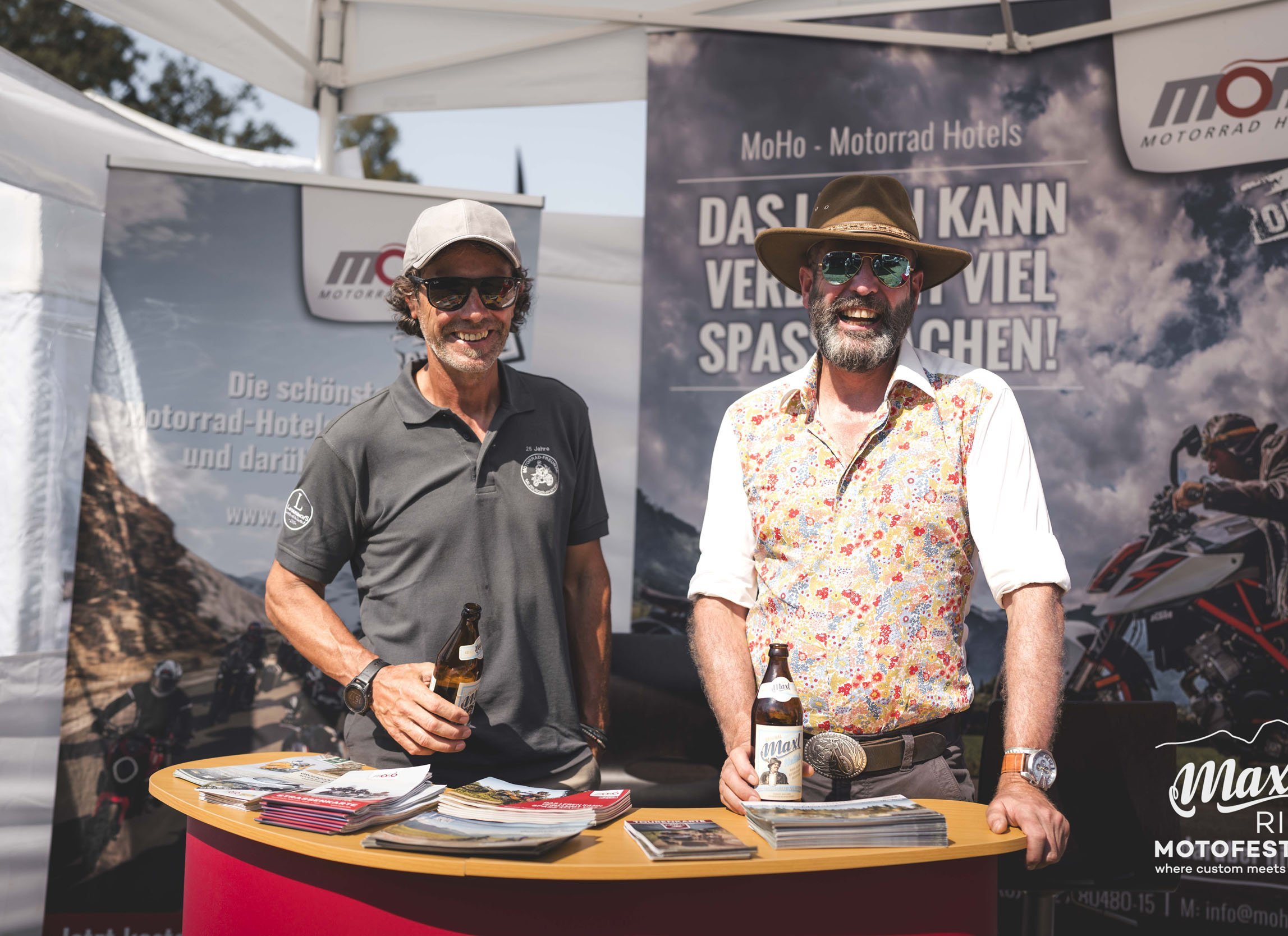 Zwei Männer stehen am Infostand mit Bierflaschen auf einem Motorradevent