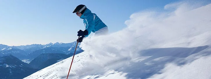 Skifahrer in blauer Jacke auf verschneitem Berg mit Alpenpanorama