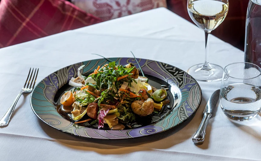 Salat mit Garnelen auf kunstvollem Teller neben Gläsern und Besteck
