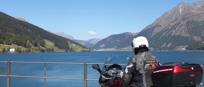 Hotel am Reschensee *** © The Dilitz Company GmbH Motorradfahrer blickt auf See und Berge bei klarem Himmel