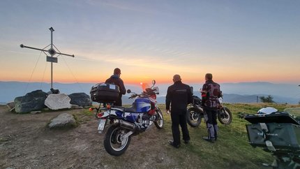 Ferienregion Wolfsberg – Region Lavanttal © Viktor Sator Drei Motorradfahrer schauen bei Sonnenuntergang vom Berggipfel mit Gipfelkreuz