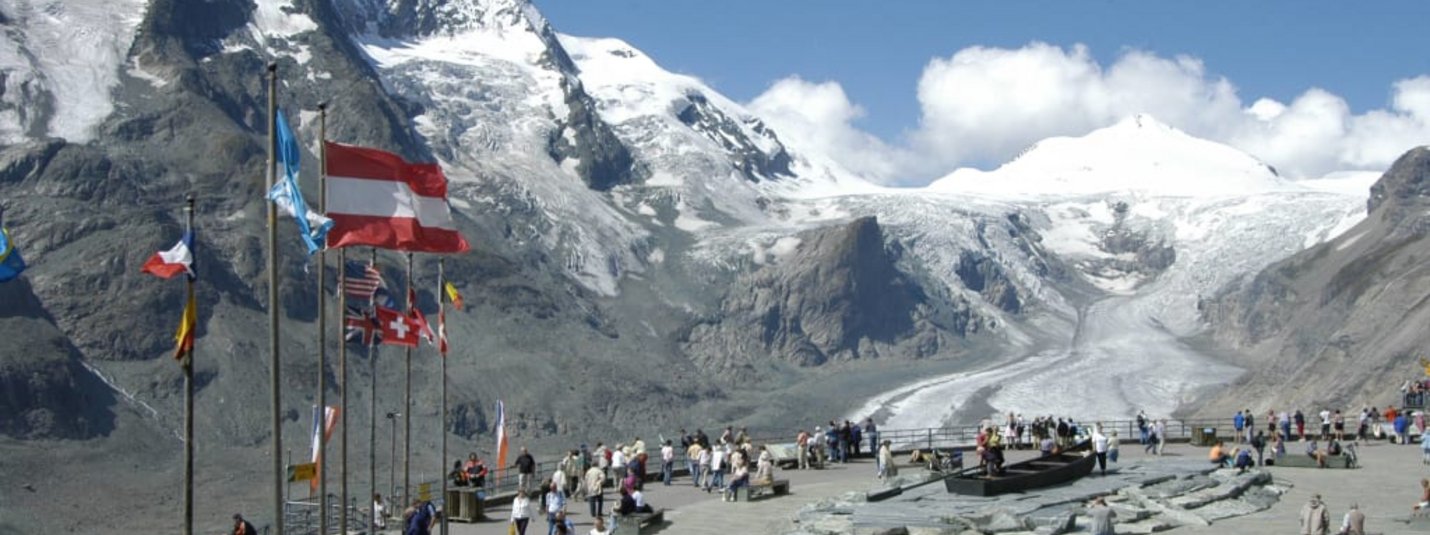 Besucher am Gletscher mit Bergpanorama und Fahnen im Hintergrund