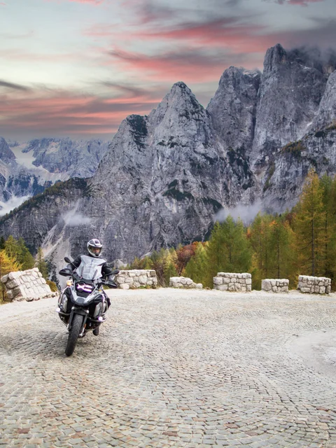 Motorcyclist on winding mountain road with rocky peaks and autumn trees