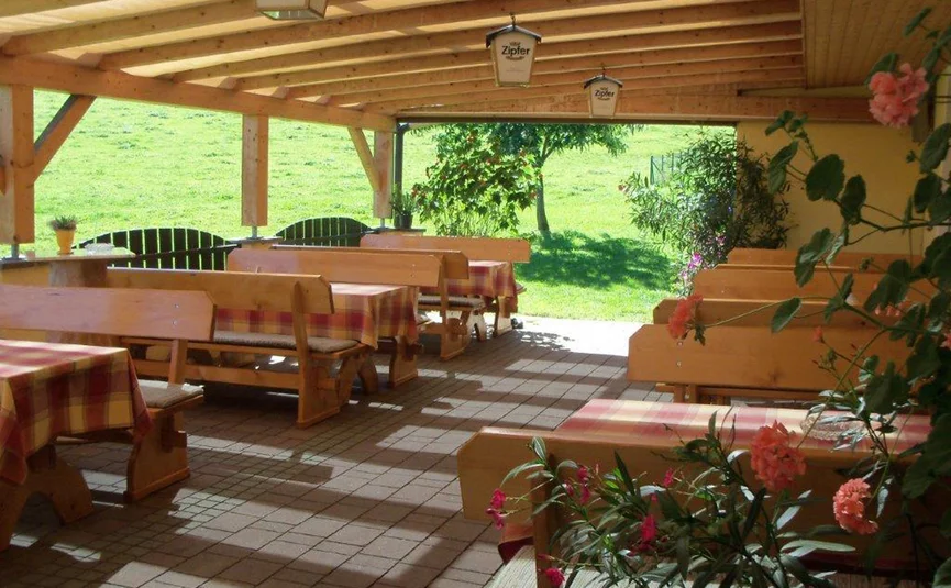 Covered patio with wooden tables, benches, and flowers overlooking green meadow