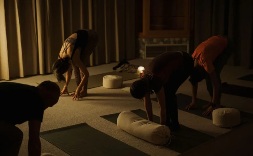 Menschen praktizieren Yoga in dunklem Raum mit Yogamatten und Kissen