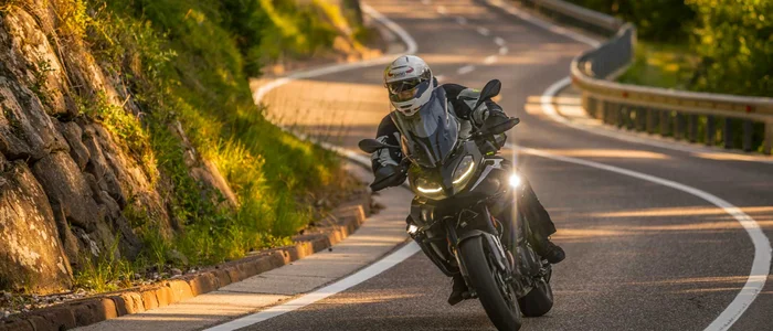 Motorrijder in beschermende kleding op kronkelende landelijke weg in zonlicht