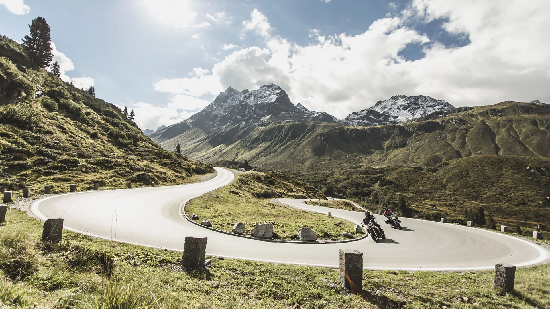 Motorcyclists riding on winding mountain road with snowy peaks