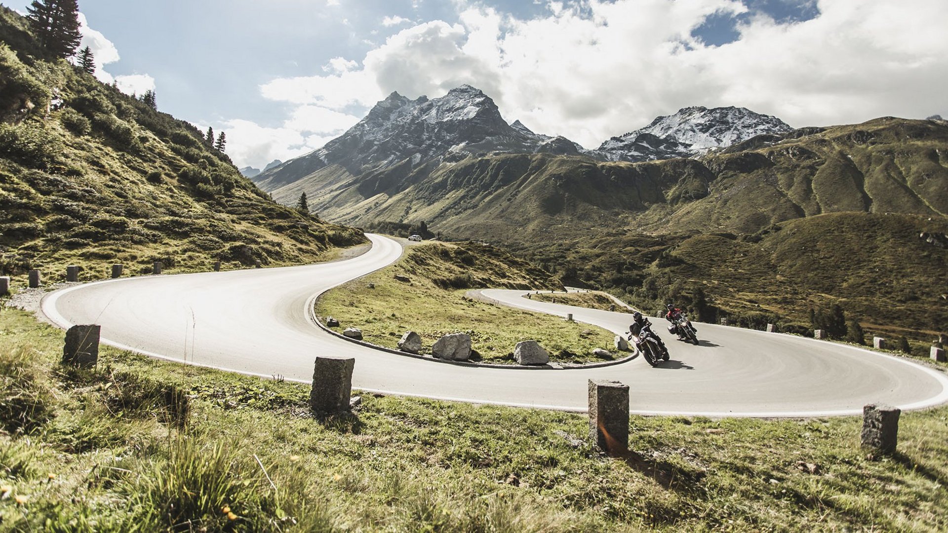 Urlaubsgutscheine © Christoph Schöch Motorradfahrer auf kurviger Bergstraße mit schneebedeckten Gipfeln
