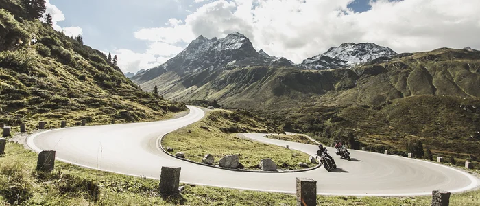 Motorradfahrer auf kurviger Bergstraße mit schneebedeckten Gipfeln