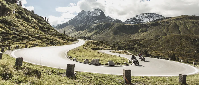 Motorradfahrer auf kurviger Bergstraße mit schneebedeckten Gipfeln