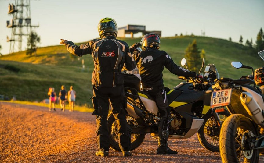 Zwei Motorradfahrer in Schutzkleidung zeigen auf einen Hügel bei Sonnenuntergang