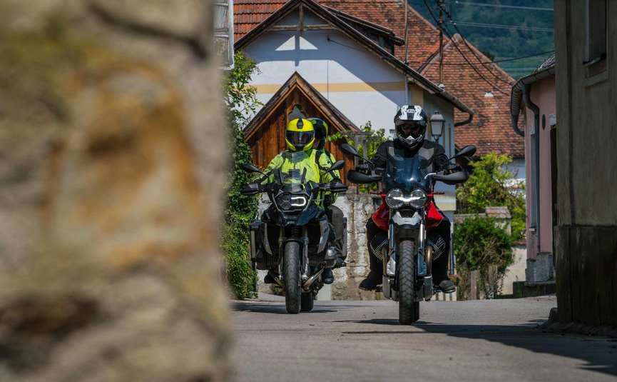 Zwei Motorradfahrer fahren durch eine kleine Gasse in einem Dorf