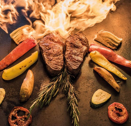 Two steaks and vegetables with flames on the grill