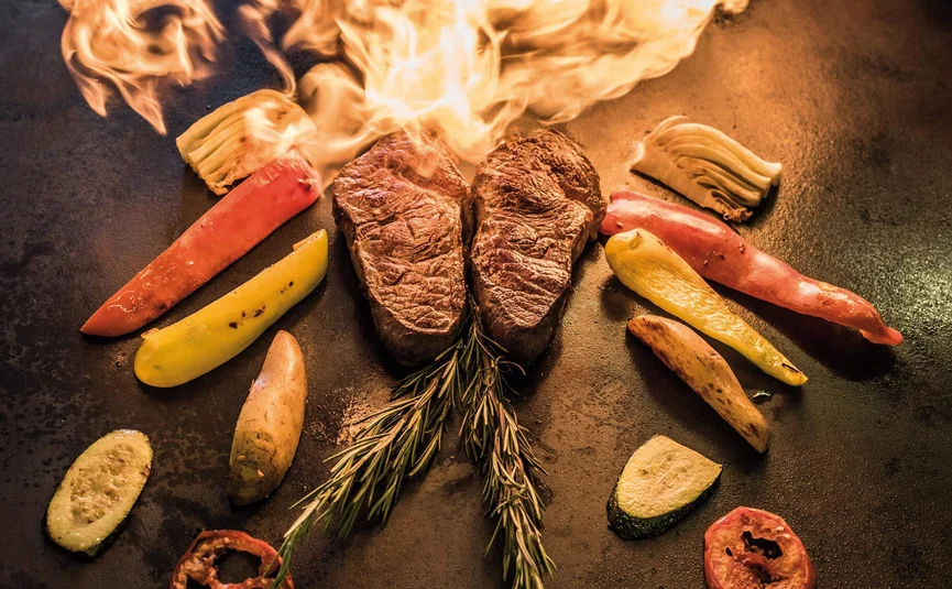 Two steaks and vegetables with flames on the grill