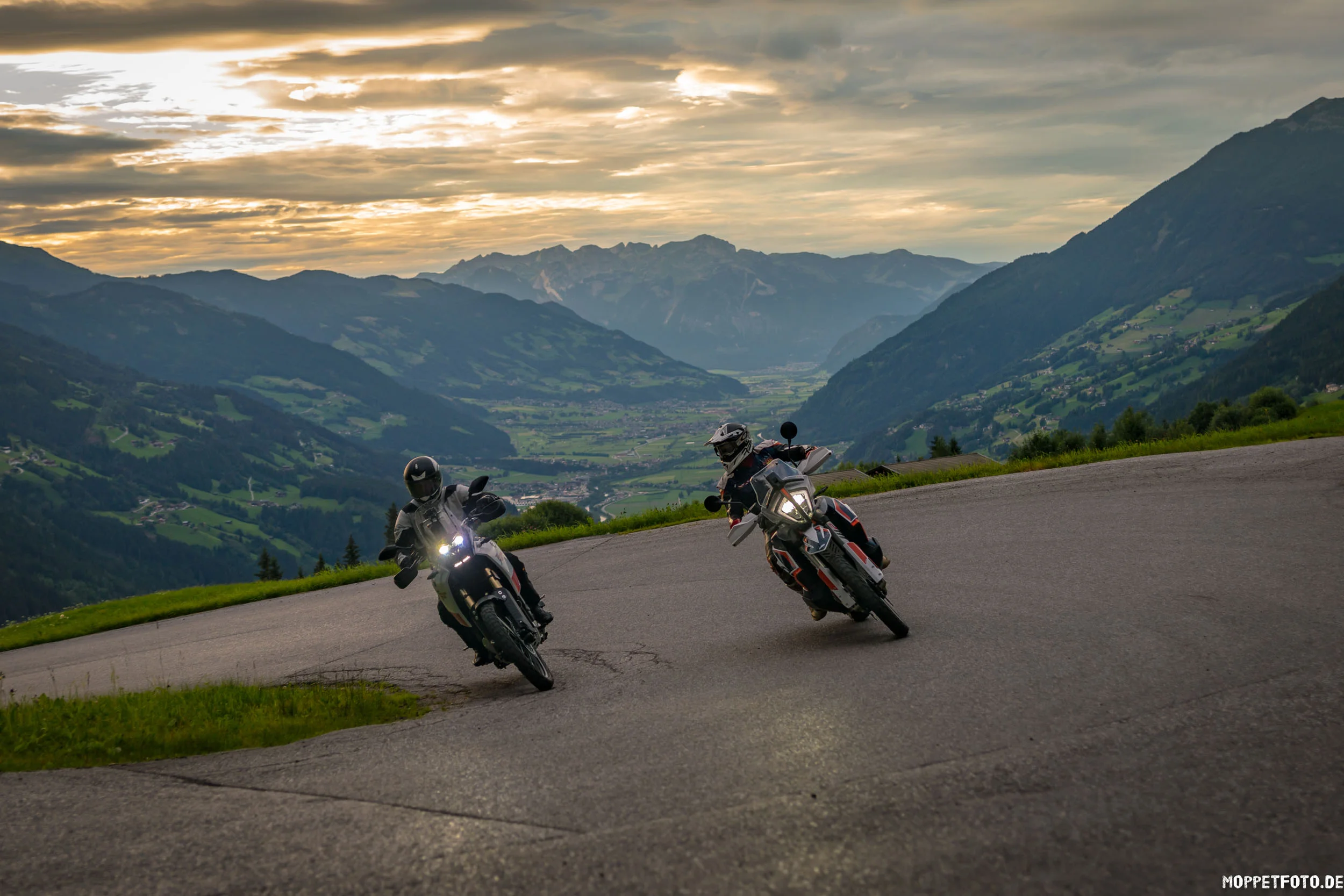 Two motorcyclists riding on winding mountain road at sunset in the Alps