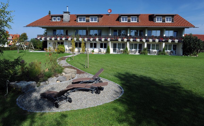 Haus mit Balkon, Blumen und Liegestühlen auf gepflegtem Grün