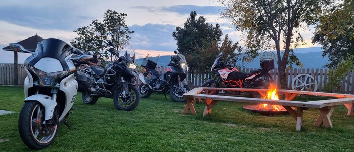 Vier Motorräder stehen auf einer Wiese neben einer Feuerstelle mit Holzbänken