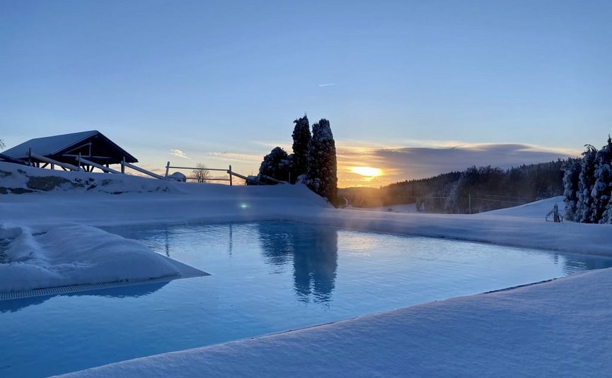 Kraftquelle Naturparadies Beheizter Außenpool mit Schnee umgeben bei Sonnenuntergang